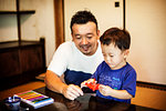Japanese man and little boy sitting at a table, making Origami animals using brightly coloured paper.