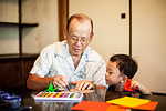 Japanese man and little boy sitting at a table, making Origami animals using brightly coloured paper.