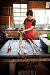 Woman standing at a table in a traditional Washi workshop, stripping bark and fibre off twigs and branches of plant material