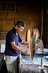 Japanese man in a workshop holding a wooden frame of dried pulp over a basin of water, making traditional Washi paper.