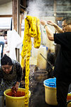 Japanese man standing in a textile plant dye workshop, holding aloft piece of freshly dyed bright yellow fabric.