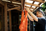 Japanese man standing outside a textile plant dye workshop, hanging up freshly dyed bright orange fabric.