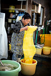 Japanese woman standing in a textile plant dye workshop, holding piece of bright yellow fabric.