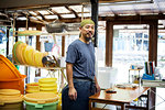 Japanese man wearing bandana standing in a textile plant dye workshop, smiling at camera.