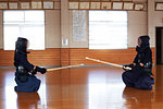 Female Japanese Kendo fighter kneeling on wooden floor, fastening