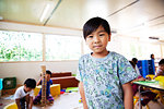 Young boy standing in a classroom in a Japanese preschool, smiling at camera.
