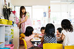 A young woman teacher and group of children in a Japanese preschool seated at a table.