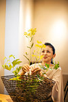 Japanese woman standing in flower gallery, working on Ikebana arrangement.