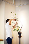 Japanese man standing in flower gallery, working on Ikebana arrangement, using secateurs.