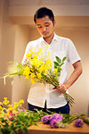 Japanese man in a flower gallery, working on Ikebana arrangement.