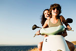 Smiling women riding scooter on beach