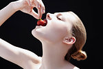 Studio shot of young woman putting strawberry into her mouth