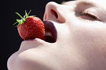 Studio head shot of young woman balancing a strawberry on lips