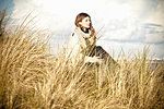 Young woman sitting in sand dunes, Bournemouth, Dorset, UK