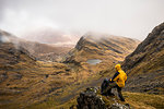 Hiker standing on a rocky outcropping of Bla Bheinn mountain, braving the wet and windy elements of the Scottish Highlands in spring, Isle of Skye, Scotland