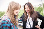 Two young female tourists giggling on Golden Jubilee footbridge, London, UK