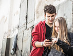 Teenage couple using smartphone by abandoned building