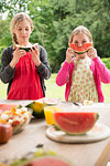 Two sisters at patio table eating and holding up watermelon slice