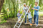 Mature man with son lifting ladder with grandsons in garden