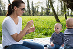 Young mother blowing bubbles for baby twin boys on picnic blanket