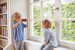 Young boy taking photograph of brother, using smartphone