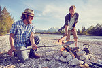 Adult men cooking fish attached to branch over campfire, Wallgau, Bavaria, Germany