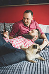 Gay couple with dog, using smartphone in bedroom