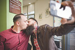 Gay couple taking selfie and kissing in cafe