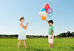 Girl taking smartphone photograph of boy holding bunch of balloons in field