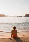 Rear view of woman sitting looking out from beach, Menorca, Balearic islands, Spain