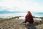 Mature woman, sitting beside lake, pensive expression