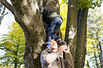 Father helping son to climb tree, looking up smiling