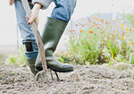 Cropped shot of woman wearing rubber boots digging organic garden with fork