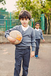 Portrait of elementary schoolboy holding soccer ball in playground