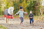 Boy and sister leading pony along country lane