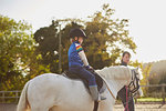 Instructor leading boy riding pony in equestrian arena