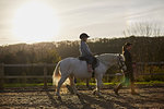 Instructor leading girl riding pony in equestrian arena