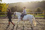 Instructor leading girl riding white pony in equestrian arena