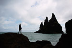Silhouette of mid adult woman standing on rock looking out to ocean, Iceland