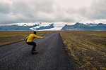 Rear view of mid adult man skateboarding to snow covered mountain range, Iceland