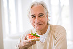 Senior man eating open sandwich in kitchen