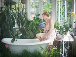 Young woman, sitting on edge of bathtub, in bathroom filled with plants