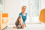 Mature woman doing stretch exercise in living room floor