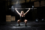 Young woman weightlifting barbell in dark crossfit gym