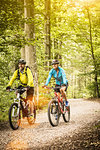 Happy mature mountain biking couple cycling on forest trail