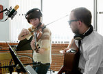 Young man and woman playing violin and guitar in music room rehearsal