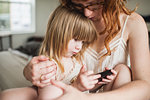 Mother hugging daughter, using smartphone