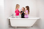 Three young girls standing in bath with lollipops