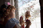 Female toddler looking out of window holding up dolls