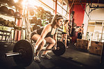 Bodybuilder bending to lift barbell in crossfit gym